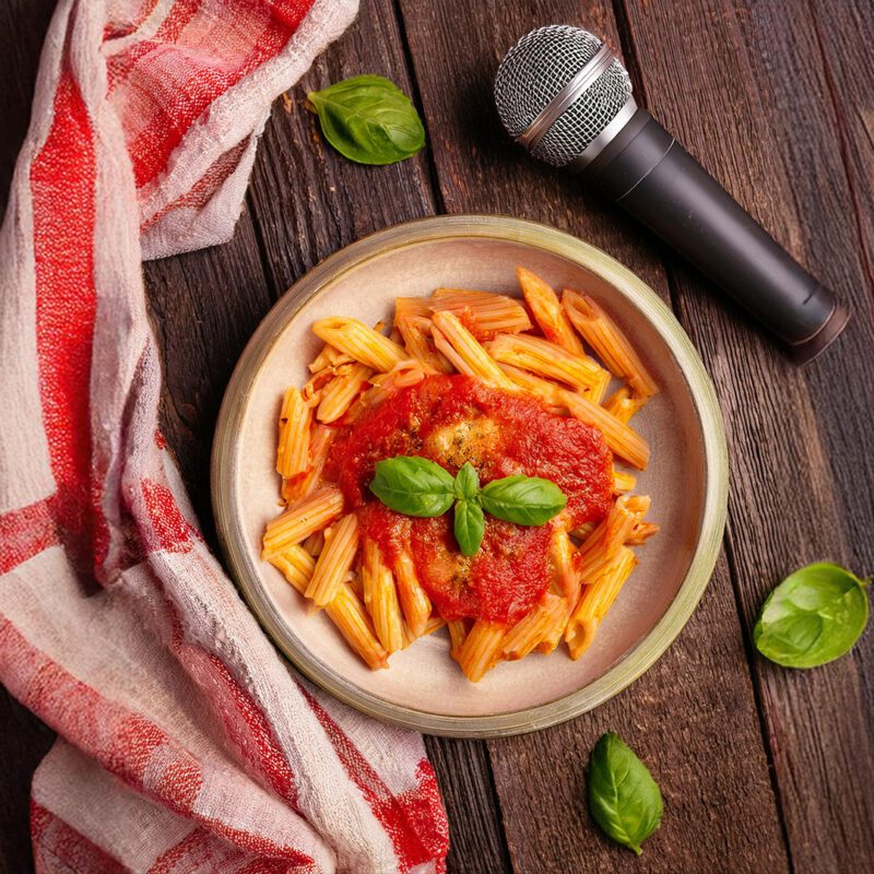 Vue plongeante sur une table en bois avec un plat de pâtes sauce tomate, un micro et un linge de cuisine.